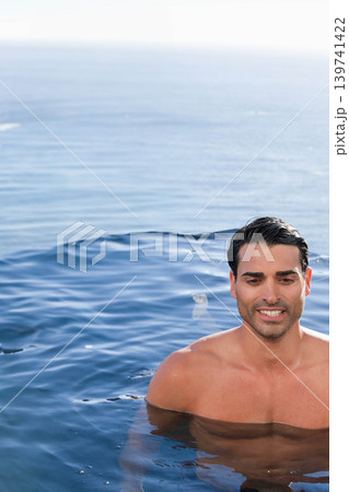 Man floating chest-deep in calm blue water near horizon, sunlit reflections, shirtless, copy space Man floating chest-deep in calm blue water near horizon, sunlit reflections, shirtless, copy space 139741422