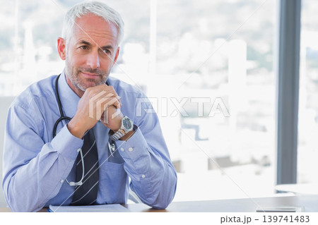 Mature male doctor sitting at desk in modern office, checking phone by documents with stethoscope 139741483