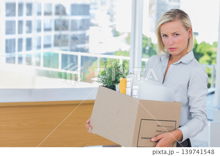 Woman in blouse and pants holding cardboard box with plant, binders at office reception, copy space Woman in blouse and pants holding cardboard box with plant, binders at office reception, copy space 139741548
