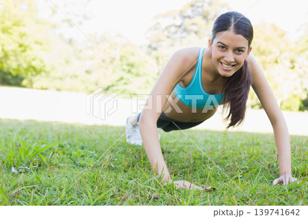 Asian female holding push-up on grassy field wearing turquoise sports bra black shorts white shoes Asian female holding push-up on grassy field wearing turquoise sports bra black shorts white shoes 139741642