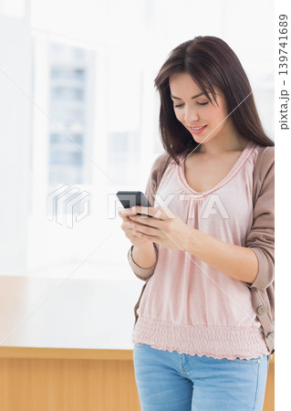 Woman wearing pink blouse checking smartphone by big windows near wooden counter, copy space Woman wearing pink blouse checking smartphone by big windows near wooden counter, copy space 139741689