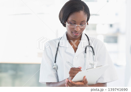 African American woman writing on clipboard with pen at clinic white coat stethoscope glasses African American woman writing on clipboard with pen at clinic white coat stethoscope glasses 139741690