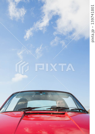 Male driver sitting behind windshield driving red convertible under blue sky with steering wheel Male driver sitting behind windshield driving red convertible under blue sky with steering wheel 139741801