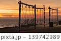 Swings on a beach are illuminated by lights as the sun sets over the sea. The sky shows warm colors while waves gently touch the shore. High quality photo 139742989