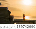 A bottle of beer on the table during sunset at sea. A man looks at the sea, rests and watches the setting sun, the concept of a holiday at a resort. Relaxing and enjoying a drink in the evening. High 139742990