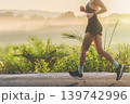 Running in nature copy space. A person runs on a road at sunrise. Mist covers the landscape, and trees are seen in the distance. The runner appears focused on their workout. High quality photo 139742996
