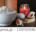 Sea salt for spa treatments is in a white ceramic bowl with a pestle on a wooden table. Burning red candle and sea shells for relaxing atmosphere of a wellness salon 139743596