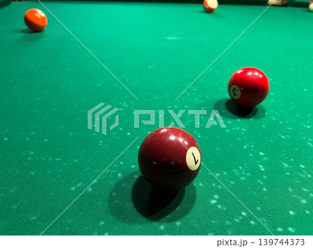Billiard table shows colorful balls scattered on green felt surface in a lively setting. Players are engaged in the game 139744373