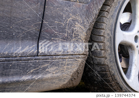 A car is stuck in mud with dirt coating its lower body and mud on the tire. The ground is soft and wet from rain A car is stuck in mud with dirt coating its lower body and mud on the tire. The ground is soft and wet from rain 139744374