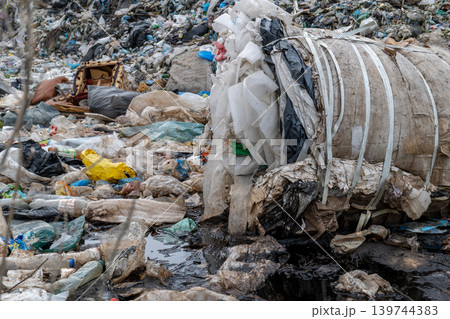 Garbage is stacked in a bale at a waste site with various types of trash scattered around. The scene shows poor waste management practices Garbage is stacked in a bale at a waste site with various types of trash scattered around. The scene shows poor waste management practices 139744383