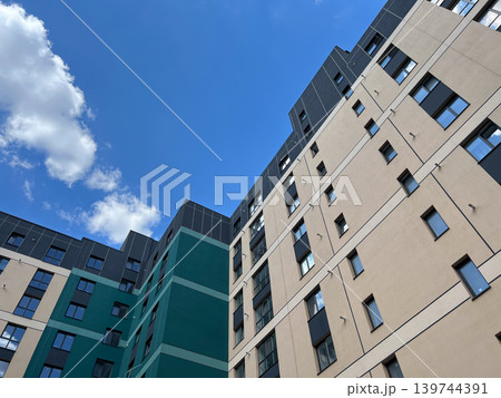 New apartment buildings stand tall against the blue sky, showcasing their unique designs under the bright sun New apartment buildings stand tall against the blue sky, showcasing their unique designs under the bright sun 139744391