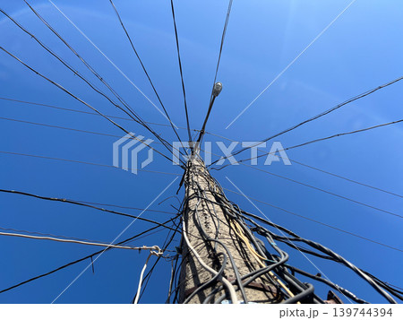 A tall utility pole stands in an open space with many wires extending in different directions under a clear blue sky A tall utility pole stands in an open space with many wires extending in different directions under a clear blue sky 139744394