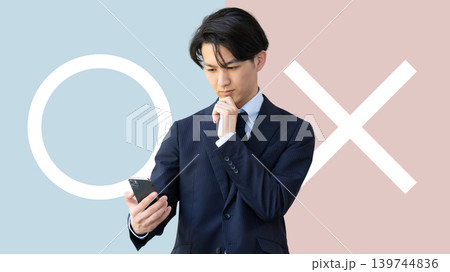 マルかバツか、スマートフォンを持って考える男性 マルかバツか、スマートフォンを持って考える男性 139744836