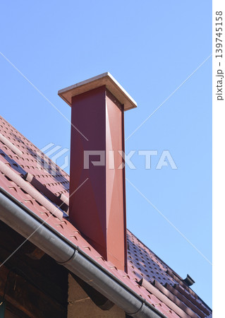 Modern metal chimney on a tiled house roof Modern metal chimney on a tiled house roof 139745158