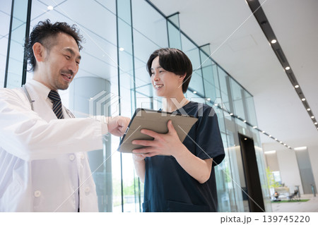 タブレットを見ながら指導や申し送りする医師と新人ドクターや看護師医療現場のDXとチーム連携イメージ 139745220