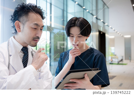 タブレットを見ながら指導や申し送りする医師と新人ドクターや看護師医療現場のDXとチーム連携考える タブレットを見ながら指導や申し送りする医師と新人ドクターや看護師医療現場のDXとチーム連携考える 139745222