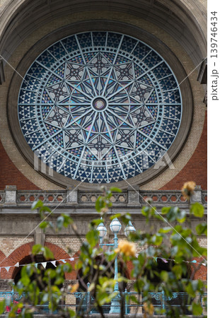 A soft foreground of green leaves and yellow roses frames an ornate Victorian lamppost, drawing the eye toward the Grade II-listed South facade of Alexandra Palace. Dominating the view is the 139746434