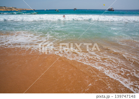 Clear turquoise water and white sea waves on sandy Red Sea beach in Sharm El Sheikh Egypt with boats in distance. Travel and resort lifestyle Clear turquoise water and white sea waves on sandy Red Sea beach in Sharm El Sheikh Egypt with boats in distance. Travel and resort lifestyle 139747148