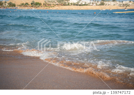 Sea waves wash sandy beach on Red Sea coast in Sharm El Sheikh Egypt with resort shoreline and sunny summer weather. Resort lifestyle and tourism Sea waves wash sandy beach on Red Sea coast in Sharm El Sheikh Egypt with resort shoreline and sunny summer weather. Resort lifestyle and tourism 139747172