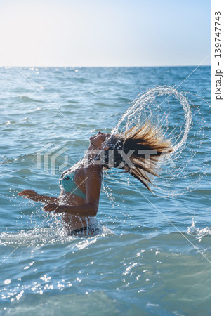 Woman flipping wet hair in sea water during sunny summer vacation 139747743
