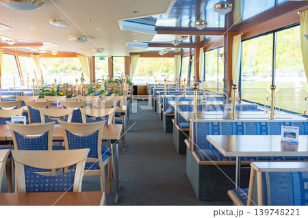 Bright restaurant interior with tables and chairs inside modern passenger cruise ship. Cozy dining area with panoramic windows and daylight. 139748221