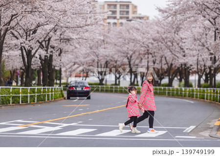 Mother and daughter crossing street under blooming cherry blossom trees in spring Mother and daughter crossing street under blooming cherry blossom trees in spring 139749199