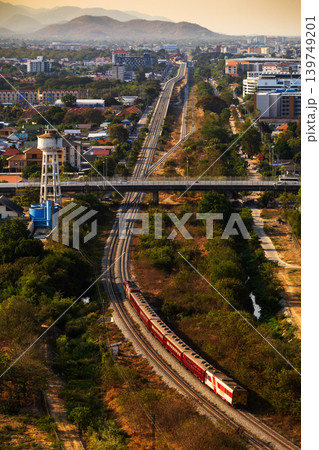 Aerial view of a red train traveling on tracks through a lush green landscape and cityscape 139749201