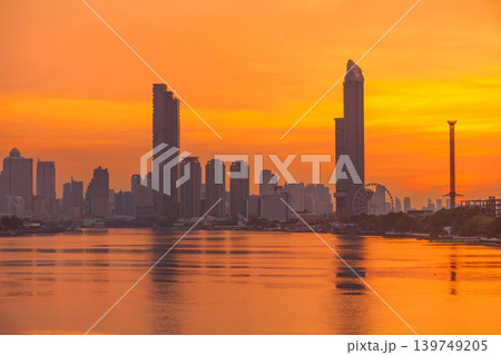 Vibrant orange sunset over a sprawling city skyline reflected in a calm river Vibrant orange sunset over a sprawling city skyline reflected in a calm river 139749205