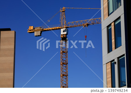Tower crane between modern buildings against clear blue sky, urban construction Tower crane between modern buildings against clear blue sky, urban construction 139749234