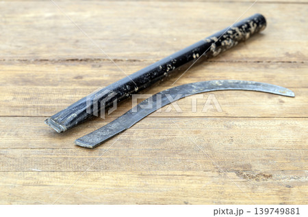 Old Broken Iron Sickle with Curved Blade Separated from Its Worn Black Handle on a Rustic Wooden Background Showing Clear Break Point and Aged Metal Texture Old Broken Iron Sickle with Curved Blade Separated from Its Worn Black Handle on a Rustic Wooden Background Showing Clear Break Point and Aged Metal Texture 139749881