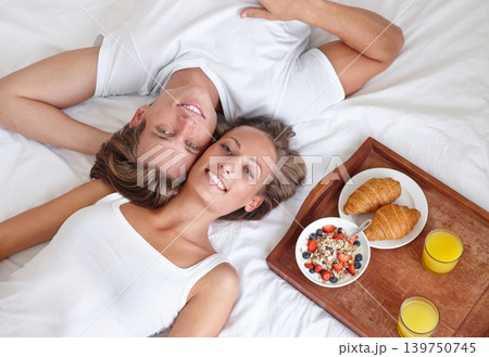 Portrait of happy couple, morning and breakfast in bed to wake up for food or meal together to relax. Man, above or woman in home eating healthy snack with smile or juice for diet for love in bedroom Portrait of happy couple, morning and breakfast in bed to wake up for food or meal together to relax. Man, above or woman in home eating healthy snack with smile or juice for diet for love in bedroom 139750745