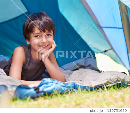 Boy, kid and camping, relax in tent and summer vacation with travel and happy in portrait outdoor. Rest on sleeping bag, young child with smile and adventure in nature, childhood and recreation 139751620