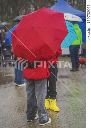 People standing under bright umbrellas during rain in public park, wet pavement, colorful rainwear, blurred background. Concept of umbrella protection, weather, season, event 139752068