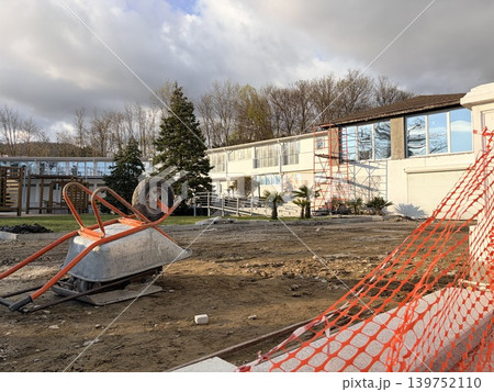 an orange-handled metal wheelbarrow lies tipped on its side on the rough, dirt-covered ground. Outdoor construction or renovation site 139752110