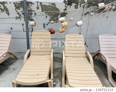 a row of beige plastic sun loungers arranged on a concrete surface, likely on a patio or terrace. a row of beige plastic sun loungers arranged on a concrete surface, likely on a patio or terrace. 139752114