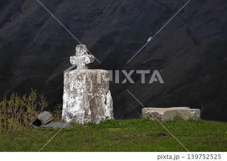 Weathered stone cross stands alone on grassy hillside 139752525