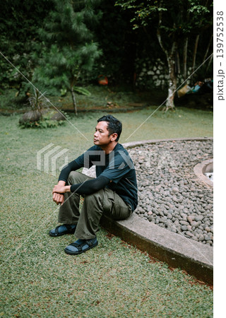 Southeast Asian Man Sitting Thoughtfully on Grass Outdoors 139752538
