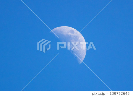 Daytime moon. Moon in the daylight. Moon during the day. White half moon visible in the daytime against a blue sky. 139752643