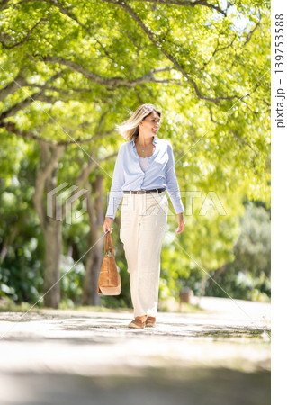 Woman walks along a path in a park under green trees during a sunny day in the afternoon 139753588