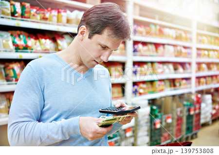 Man with dollars and calculator in store Man with dollars and calculator in store 139753808