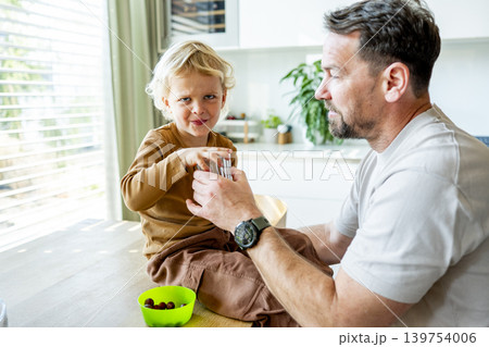 Dad feeding toddler during family mealtime in modern kitchen. Dad feeding toddler during family mealtime in modern kitchen. 139754006