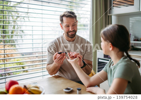 Father checking blood sugar level of diabetic teenage daughter using glucose meter. Father checking blood sugar level of diabetic teenage daughter using glucose meter. 139754028