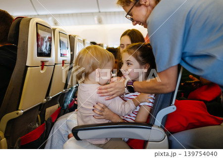Older sister entertaining toddler sibling while sitting together on airplane seat. 139754040