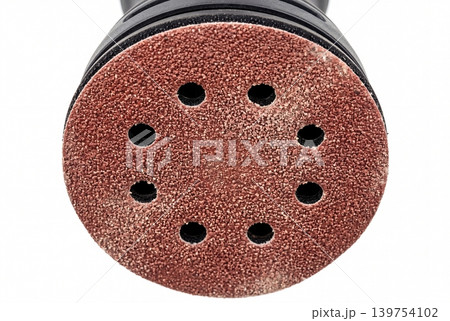 Macro close-up of an orbital sander sanding disc with dust extraction holes, isolated on a white background. Ideal for themes of woodworking, surface preparation, renovation, finishing. Macro close-up of an orbital sander sanding disc with dust extraction holes, isolated on a white background. Ideal for themes of woodworking, surface preparation, renovation, finishing. 139754102