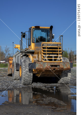 Yellow wheel loader front end on muddy construction site against blue sky Yellow wheel loader front end on muddy construction site against blue sky 139754145