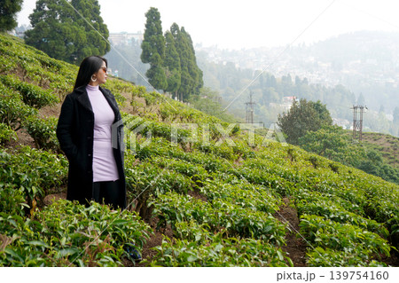 Side profile of an elegant young woman standing in a mountain tea garden looking at the distant hill town 139754160