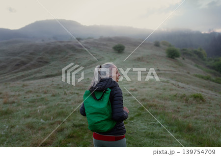 Senior woman hiking in nature on early morning with fog and mountains in background. Senior woman hiking in nature on early morning with fog and mountains in background. 139754709