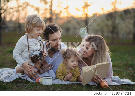 Family having picnic in spring nature, reading book on picnic blanket. 139754721