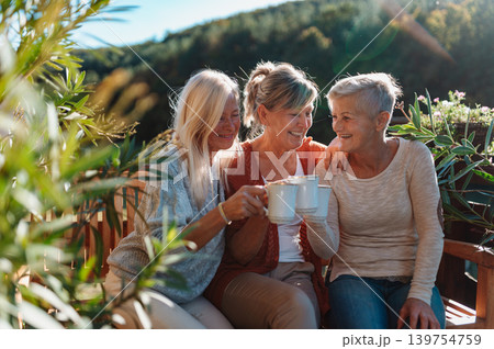Senior female friends enjoying coffee together on cabin terrace getaway. Senior female friends enjoying coffee together on cabin terrace getaway. 139754759