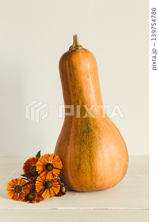 Ripe orange pumpkin on a pastel beige background with flowers of Helenium autumnale. Thanksgiving card or background. 139754780